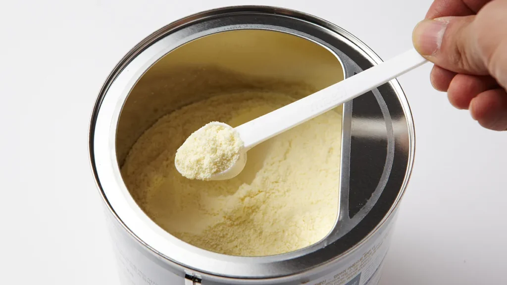 A scoop of powdered infant formula being lifted from a tin