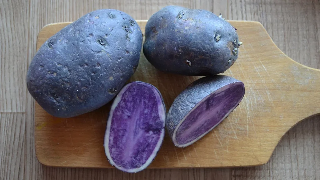 Purple-fleshed potatoes, whole and cut open, on a wooden board