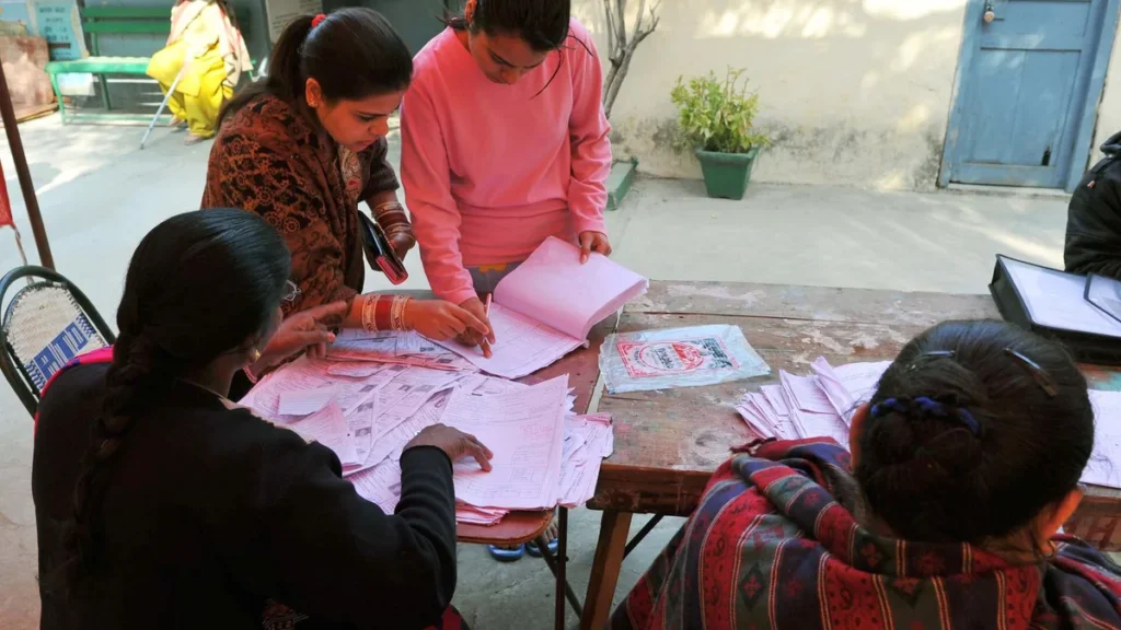 People checking names in printed voter lists at a table