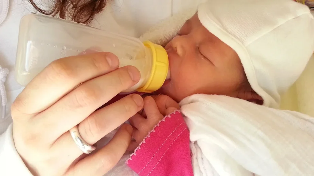 An infant drinking milk from a feeding bottle