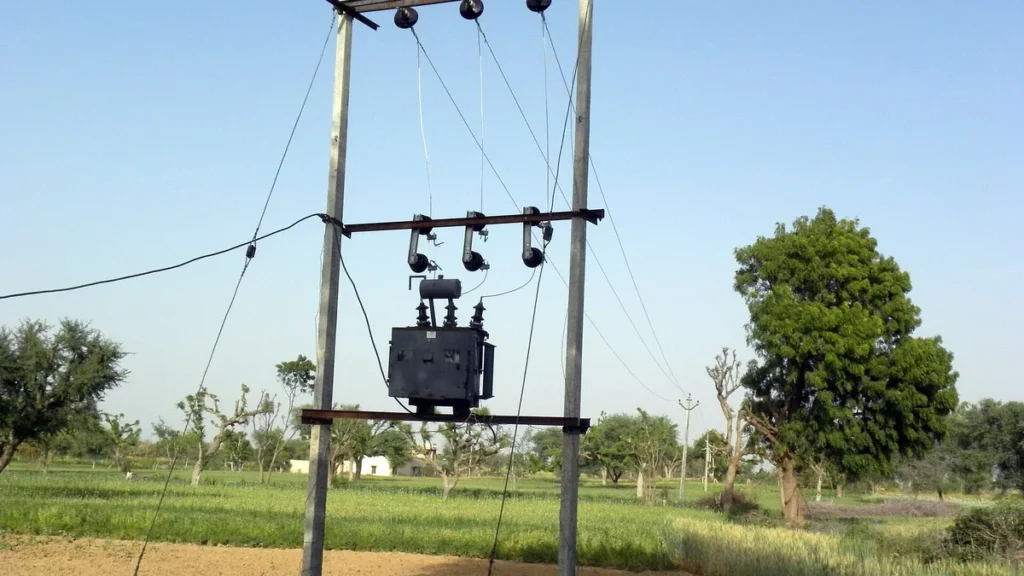 A three-phase electricity distribution transformer on poles beside farmland