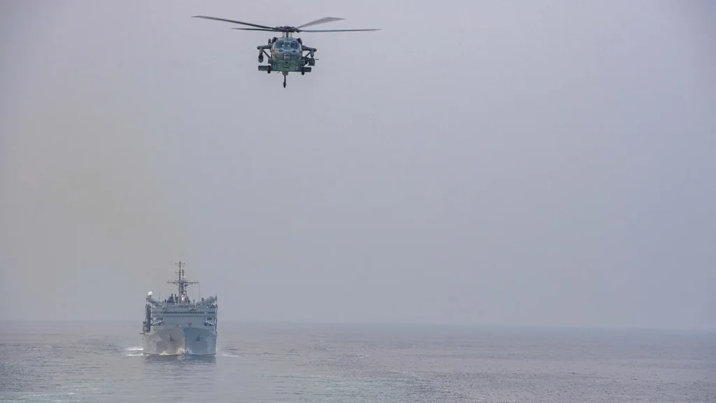 A U.S. Navy ship and helicopter transiting the Strait of Hormuz between the Persian Gulf and the Gulf of Oman