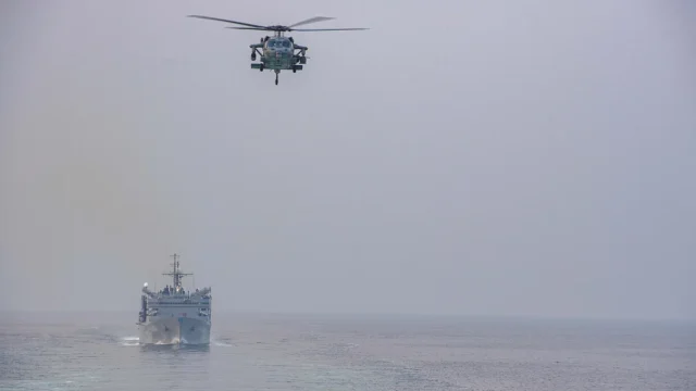 A U.S. Navy ship and helicopter transiting the Strait of Hormuz between the Persian Gulf and the Gulf of Oman