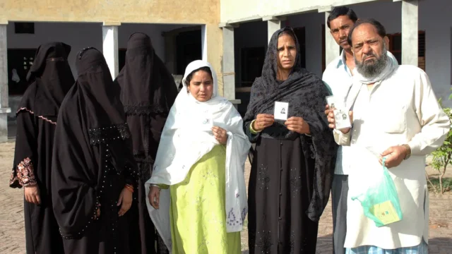 Voters showing their voter identity cards in a queue at a polling booth in Baghpat, Uttar Pradesh
