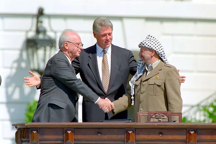 Yitzhak Rabin and Yasser Arafat shake hands, with Bill Clinton, after the Oslo signing, 13 September