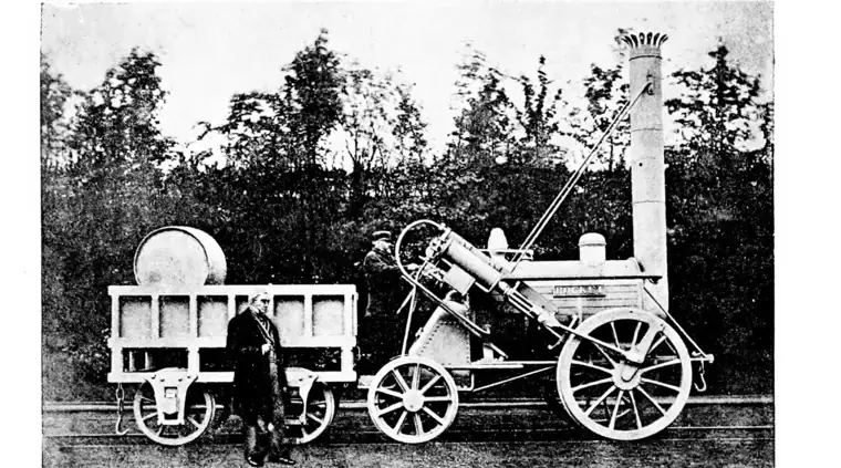 Old photograph of Stephenson's Rocket steam locomotive with its tall chimney, large driving wheels and tender, on rails